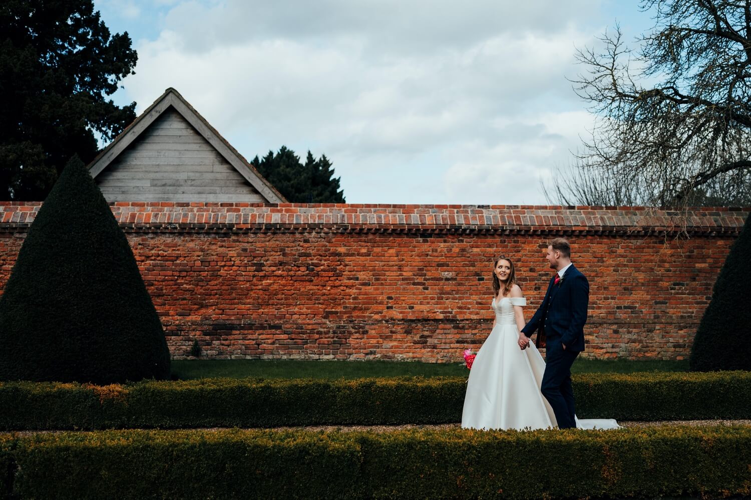 Bride and groom walking through grounds of Doddington Hall
