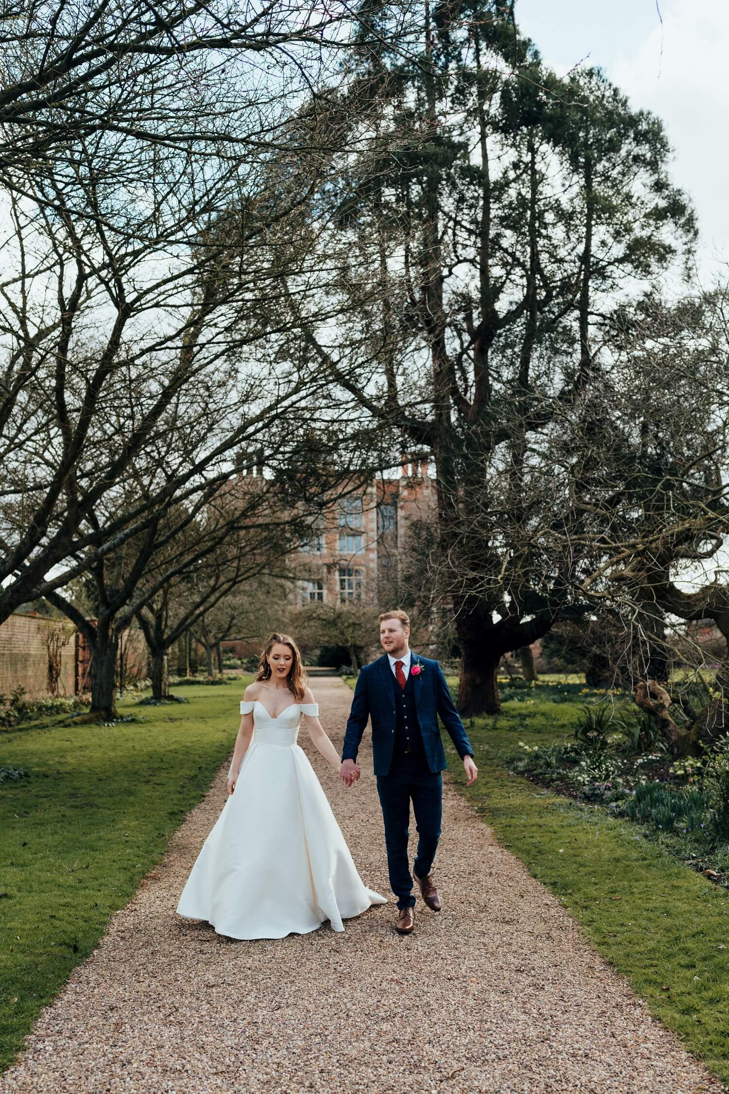 Bride and groom walking through grounds of Doddington Hall