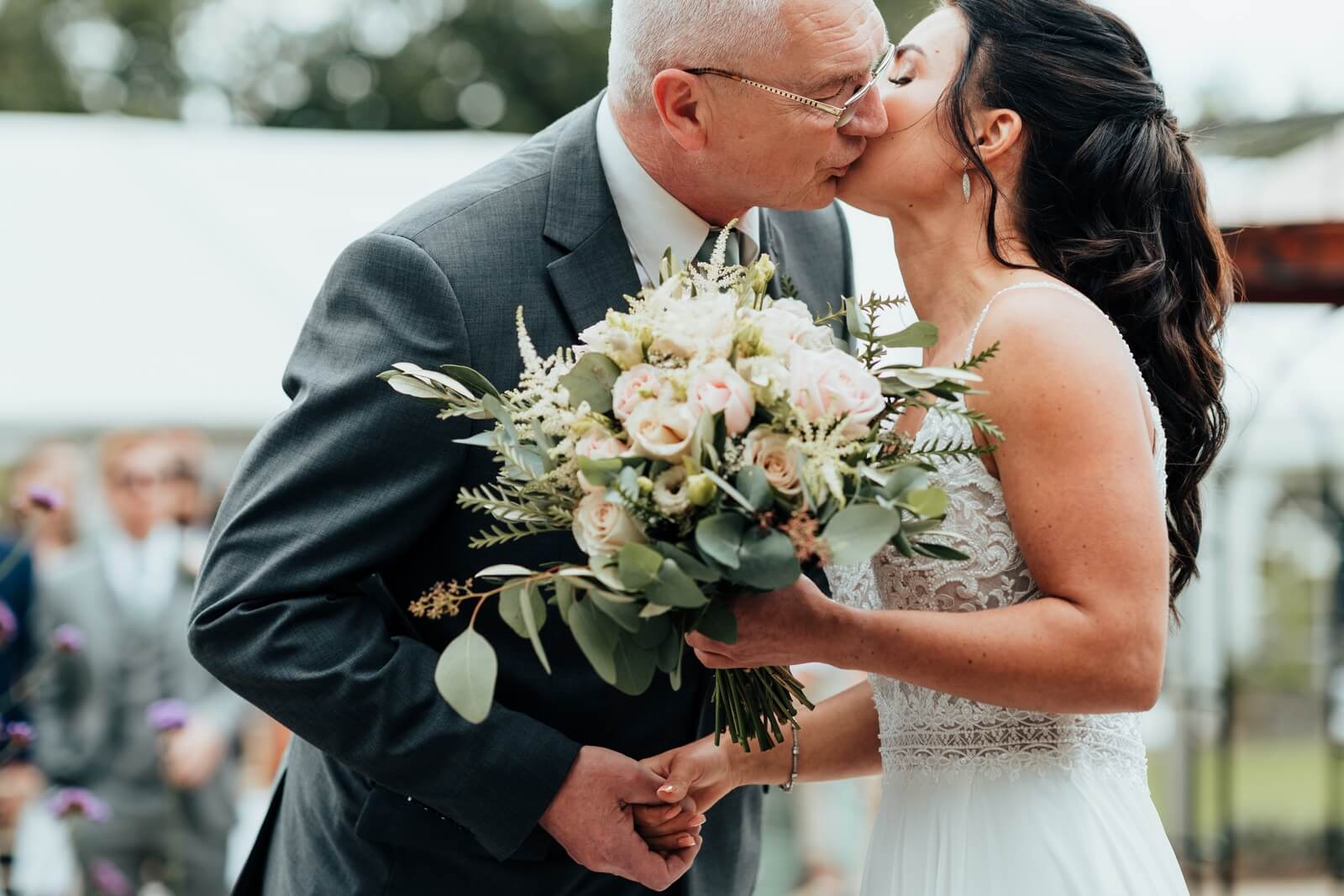 Father of the bride kiss at opening to walled garden wedding ceremony